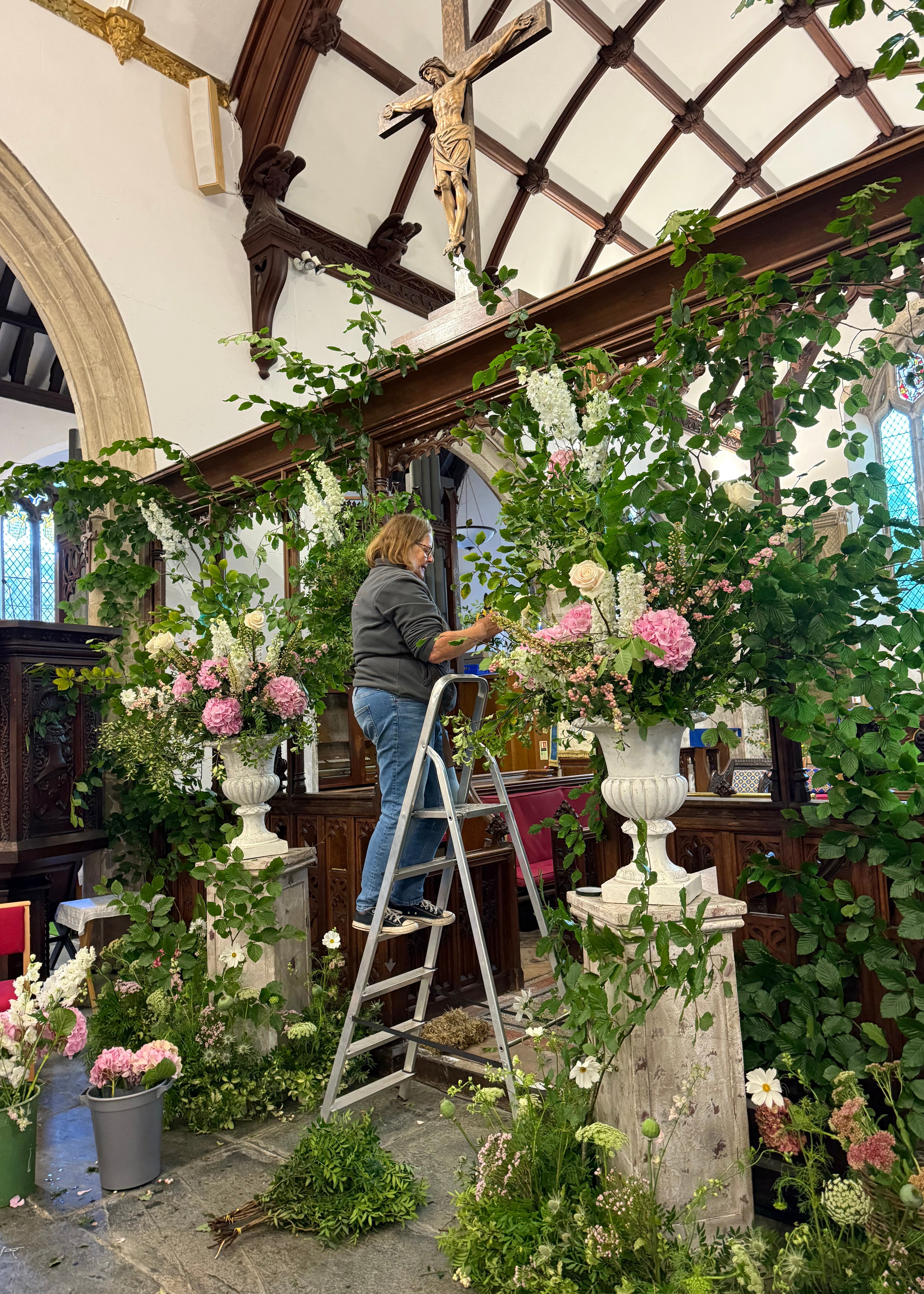 Person working on floral arrangements inside a building with wooden beams and large windows.